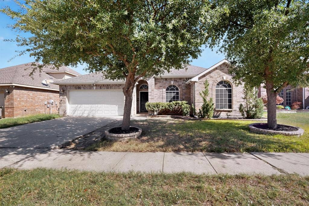 14908 Riverside Drive, Little Elm, TX 75068 Brick veneer exterior with arched windows, an attached two-car garage, and mature trees
