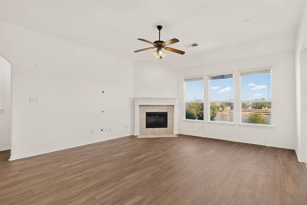 14908 Riverside Drive, Little Elm, TX 75068 Spacious living area featuring wood-finish flooring, a ceiling fan with brushed metal finish, and a fireplace with stone surround