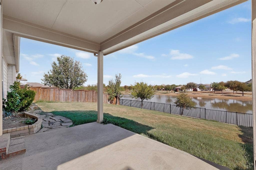 14908 Riverside Drive, Little Elm, TX 75068 Covered patio with concrete flooring, stone-lined landscaping, and a fenced backyard overlooking a body of water
