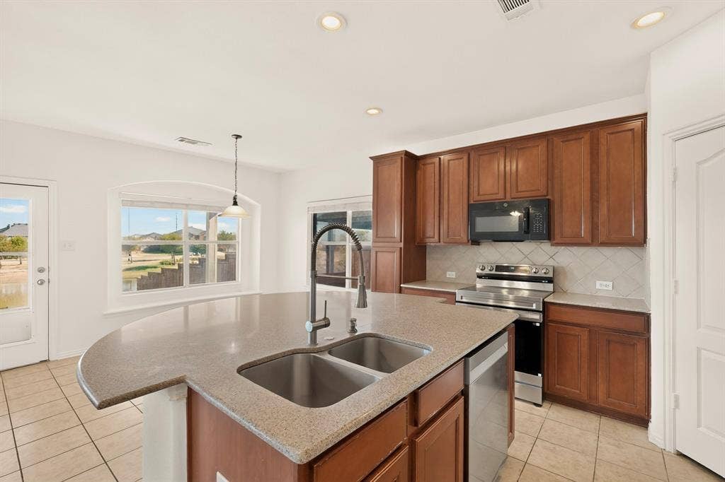 14908 Riverside Drive, Little Elm, TX 75068 Kitchen featuring a curved island with integrated double sink, wood cabinetry, stainless steel appliances, and a tiled backsplash