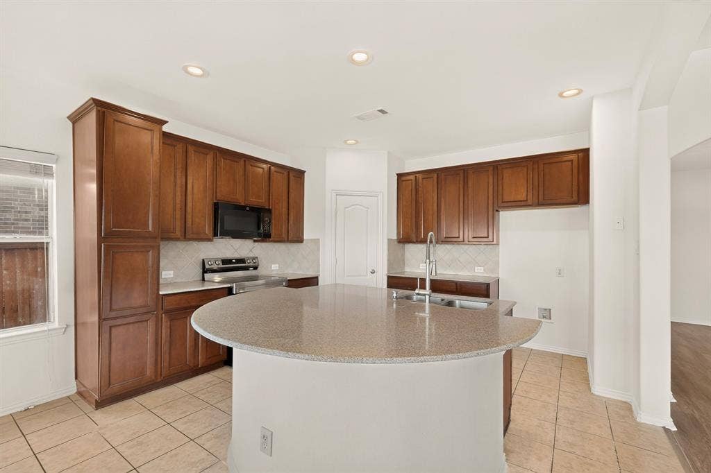 14908 Riverside Drive, Little Elm, TX 75068 Recessed lighting illuminates a kitchen featuring a curved island with a double basin sink, wood-finish cabinetry, and stainless steel appliances