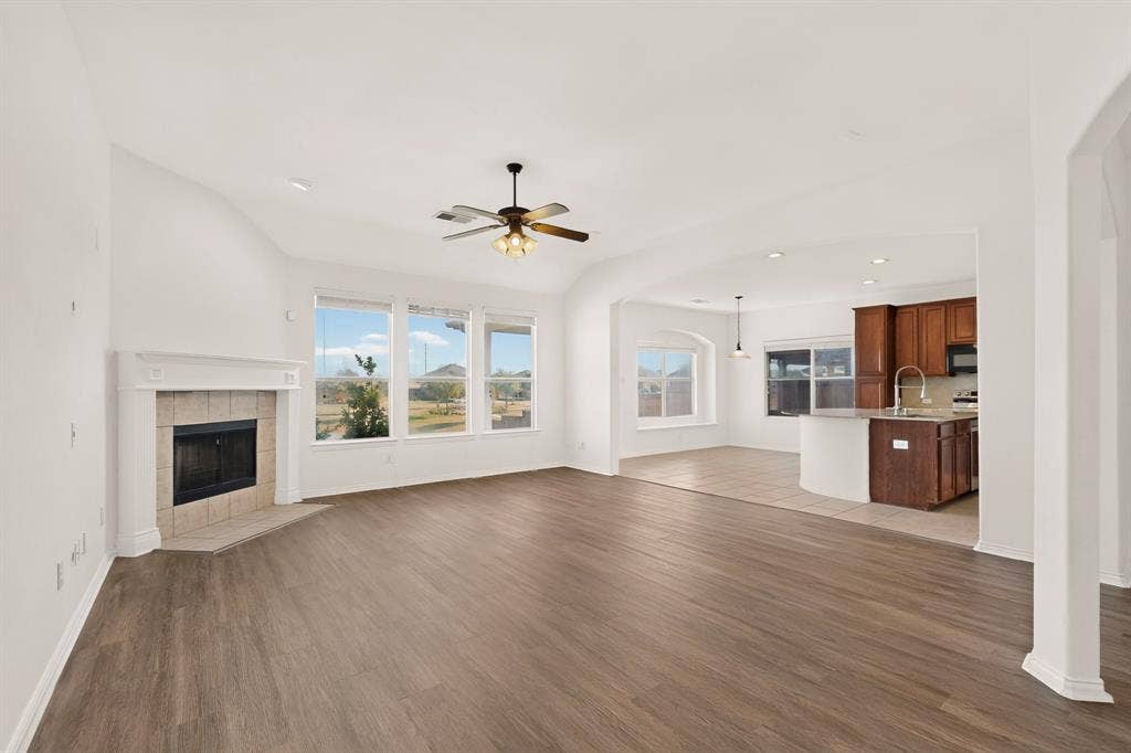 14908 Riverside Drive, Little Elm, TX 75068 Spacious living area featuring wood-finish flooring, a corner fireplace with a tiled surround, and multiple large windows