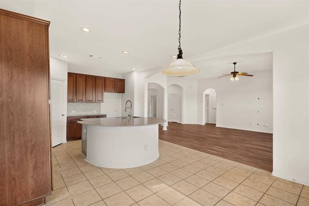 14908 Riverside Drive, Little Elm, TX 75068 Kitchen featuring wood-finish cabinetry, tile flooring, recessed lighting, and a curved island with an undermount sink