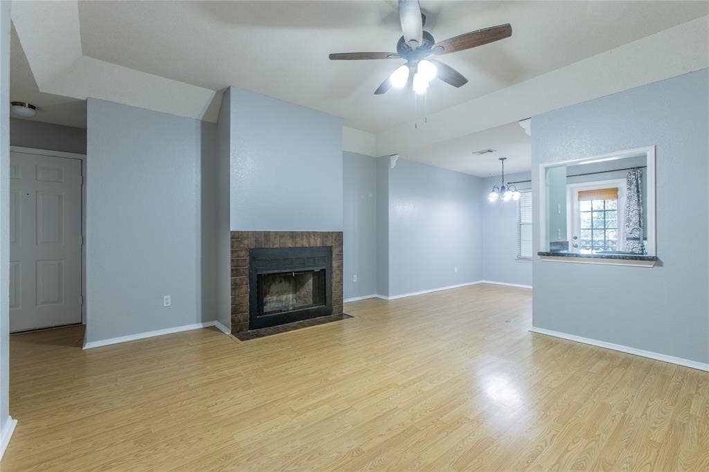 2308 Melissa Drive, #H5, Waco, TX 76708 Living area featuring wood-finish flooring, a ceiling fan with integrated lighting, a fireplace with a tile surround, and a pass-through window with a countertop