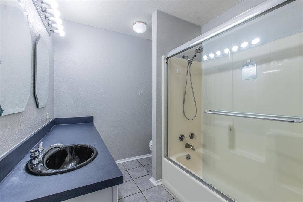 2308 Melissa Drive, #H5, Waco, TX 76708 Bathroom with tile flooring, a dark countertop vanity, black oval sink, and a combination shower/tub with sliding glass doors