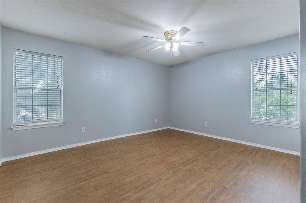 2308 Melissa Drive, #H5, Waco, TX 76708 Spacious interior with wood-finish flooring, two windows with blinds, a ceiling fan, and light gray walls