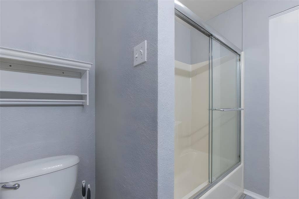 2308 Melissa Drive, #H5, Waco, TX 76708 Bathtub with a sliding glass enclosure, integrated shelving, and a toilet