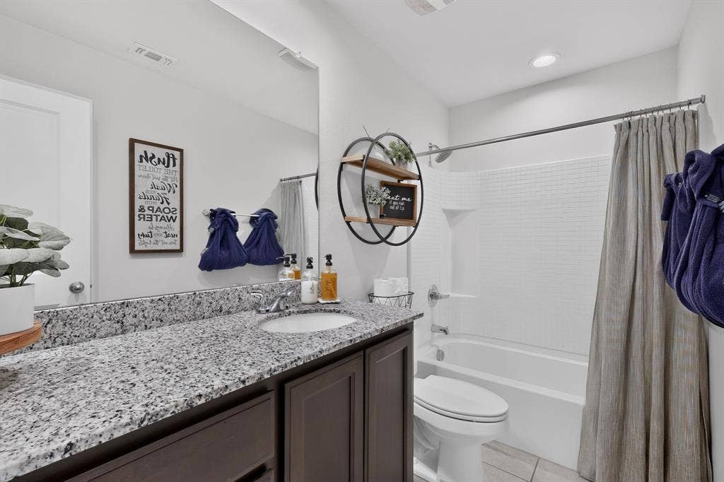 11700 Aldermoor Court, Fort Worth, TX 76036 Granite-style countertop with integrated sink, dark wood-finish vanity with cabinet storage, and a white tiled shower/tub combination