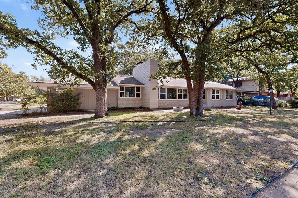 2314 Wales Place, Irving, TX 75062 Single-story residence featuring a neutral exterior, multiple windows, and a prominent chimney structure