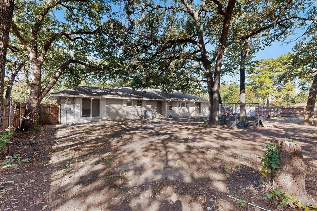 2314 Wales Place, Irving, TX 75062 Expansive rear yard with mature trees, fenced perimeter, and a light-colored exterior with sliding glass doors
