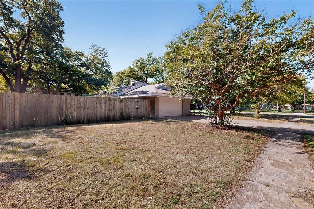 2314 Wales Place, Irving, TX 75062 Enclosed backyard featuring a tall wooden fence, mature trees, and a concrete driveway leading to the garage