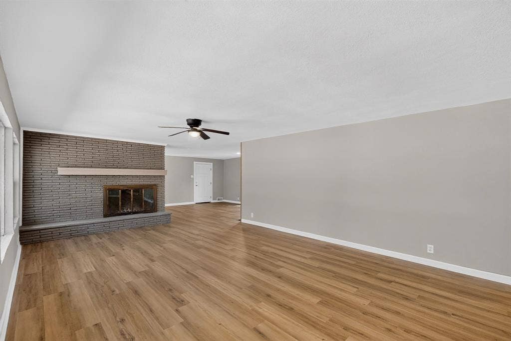 2314 Wales Place, Irving, TX 75062 Expansive room with wood-finish flooring, a brick fireplace with a wood mantle, and a ceiling fan