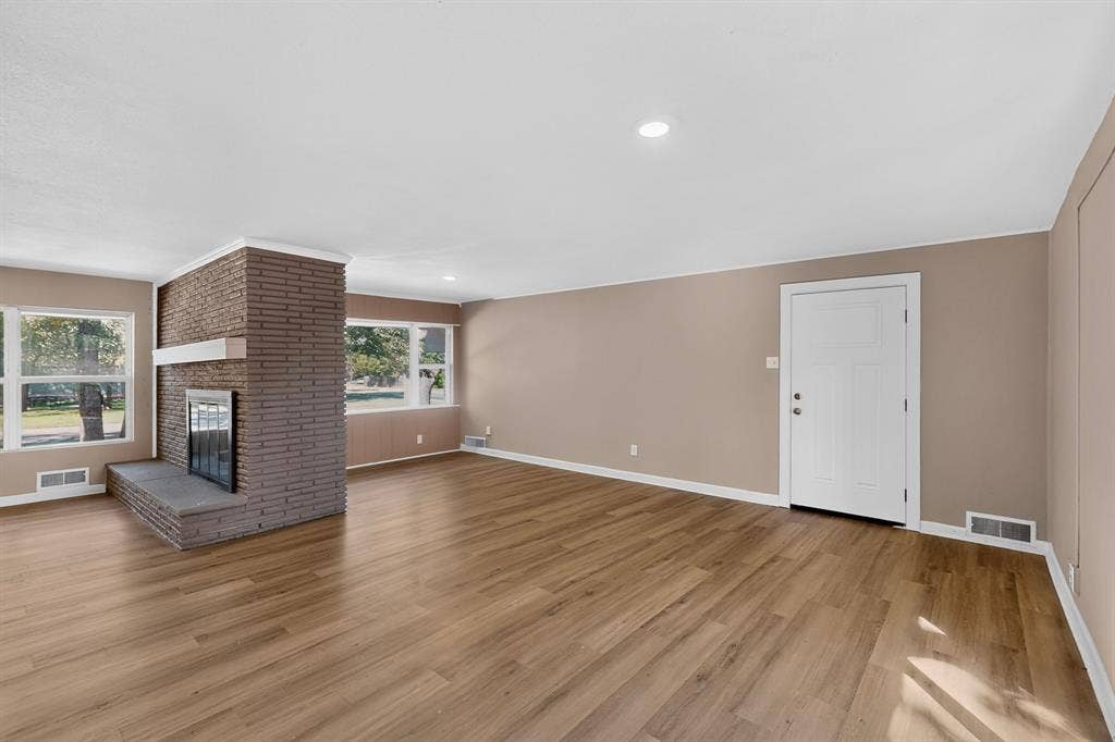 2314 Wales Place, Irving, TX 75062 Spacious interior with wood-finish flooring, a brick fireplace with a stone hearth, recessed lighting, and multiple windows