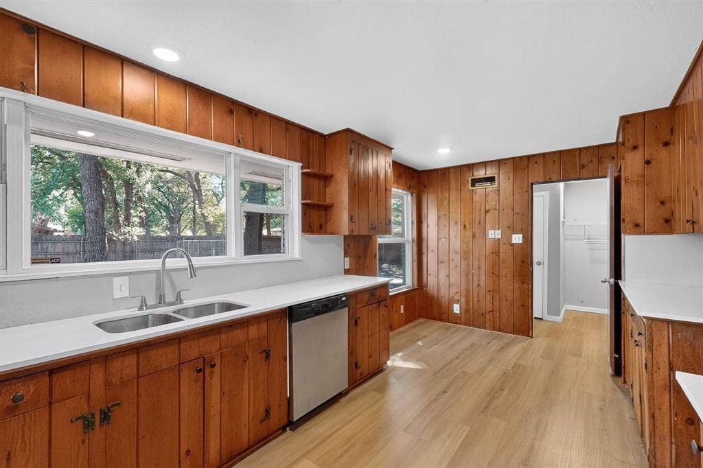 2314 Wales Place, Irving, TX 75062 Kitchen featuring wood-paneled walls, wood-finish flooring, white countertops, and a dual basin stainless steel sink with a gooseneck faucet