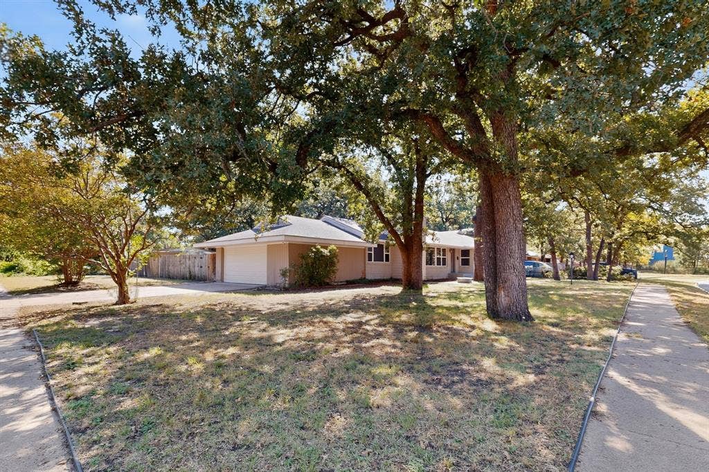2314 Wales Place, Irving, TX 75062 Single-story residence featuring a two-car garage, mature shade trees, and a concrete pathway