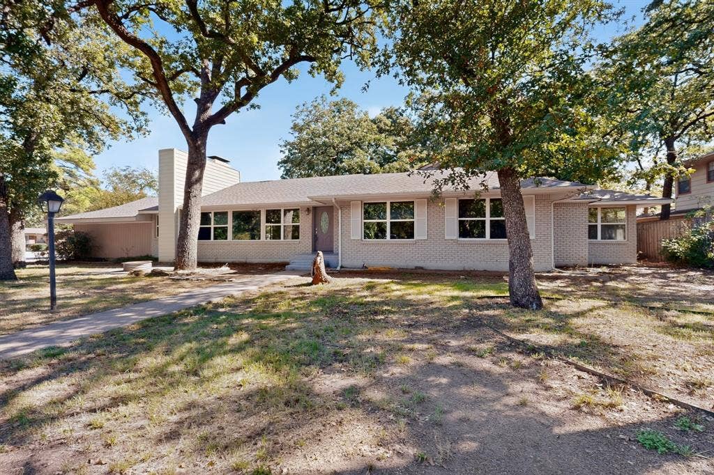 2314 Wales Place, Irving, TX 75062 Single-story residence featuring a brick facade, multiple windows, an exterior chimney, and a paved walkway