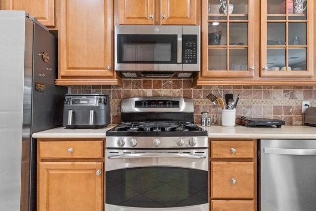 7944 Eddie Drive, Plano, TX 75025 Stainless steel gas range, stainless steel microwave, stone tile backsplash, light wood cabinetry, and stainless steel dishwasher