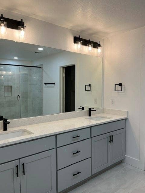 9473 Timberleaf Drive, Dallas, TX 75243 Dual vanity with light gray cabinetry, integrated sinks, white countertops, and matte black fixtures