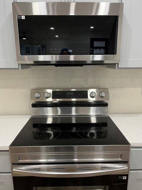 9473 Timberleaf Drive, Dallas, TX 75243 Stainless steel over-the-range microwave and electric range with a black ceramic cooktop, set against a subway tile backsplash and light-toned countertops