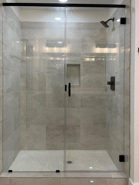 9473 Timberleaf Drive, Dallas, TX 75243 Glass-enclosed shower with matte black fixtures, a tiled shower niche, and a contrasting hexagonal tile floor