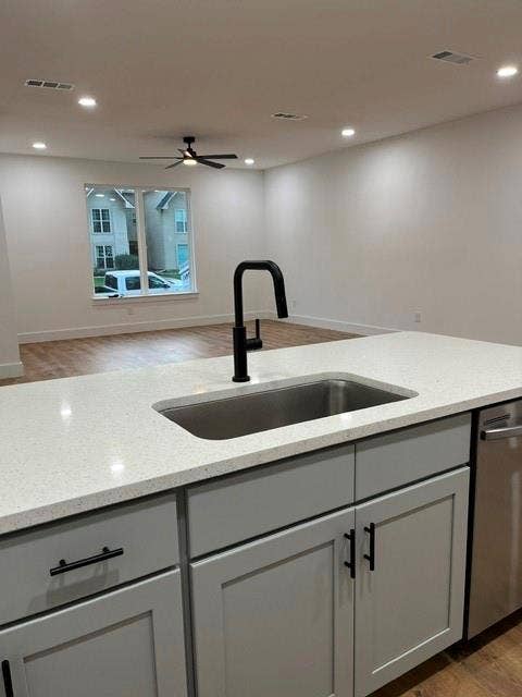 9473 Timberleaf Drive, Dallas, TX 75243 Kitchen island featuring a stainless steel undermount sink, matte black faucet, light gray cabinetry with black hardware, and an integrated dishwasher