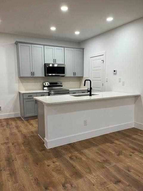 9473 Timberleaf Drive, Dallas, TX 75243 Modern kitchen featuring recessed lighting, wood-finish flooring, a kitchen island with an integrated sink, light-toned cabinetry, and stainless steel appliances