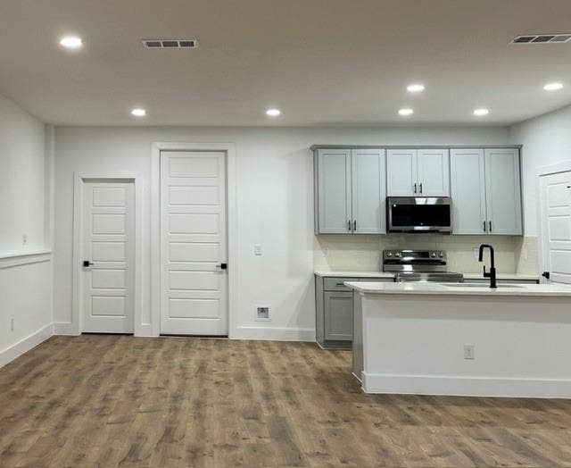 9473 Timberleaf Drive, Dallas, TX 75243 Kitchen area featuring light gray cabinetry, stainless steel appliances, a white island with a matte black faucet, and wood-finish flooring