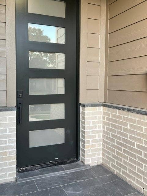 9473 Timberleaf Drive, Dallas, TX 75243 Modern entry door with five rectangular lites, complemented by light-toned brickwork and gray horizontal siding