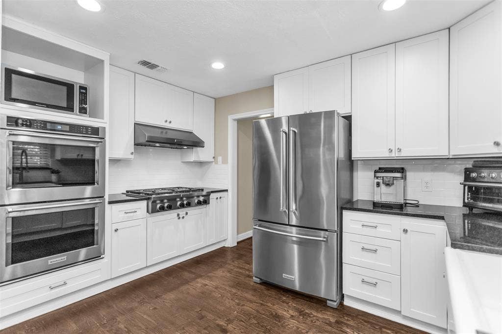 Kitchen featuring white cabinetry, dark countertops, wood-finish flooring, stainless steel appliances, and a tile backsplash