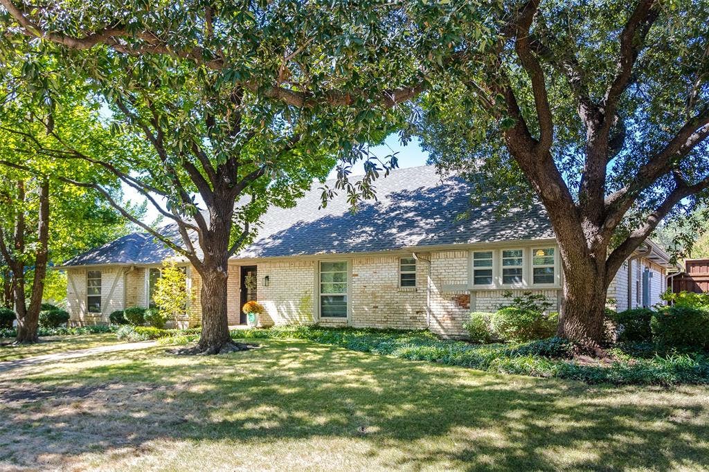Brick exterior with white mortar, dark shingle roof, and established trees providing natural shade