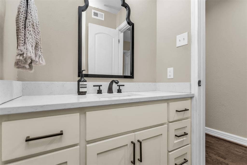 Bathroom vanity featuring a light-toned countertop with integrated sink, matte black faucet, and cream-colored cabinetry with dark hardware