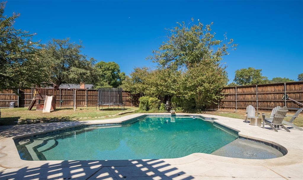 Resort-style in-ground swimming pool with sun shelf and spa, surrounded by mature landscaping and wood privacy fencing.  The large backyard makes you feel you're in the country!