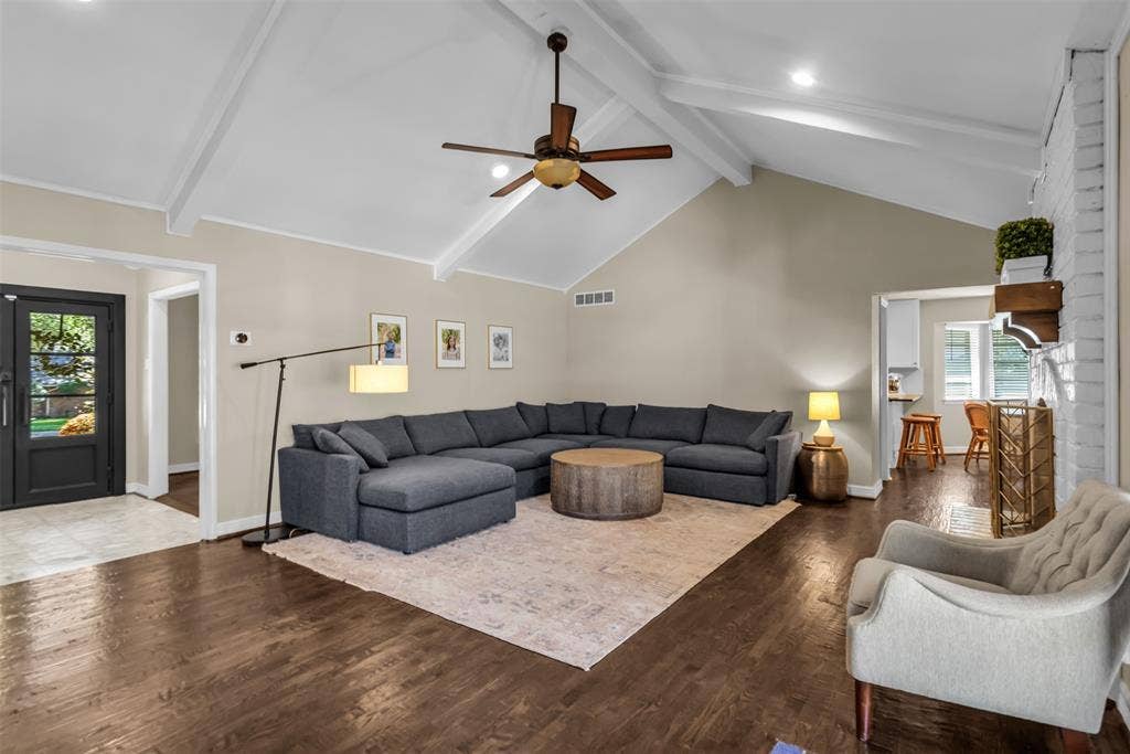 Spacious great room showcasing soaring vaulted ceilings with exposed white beams, wood-finish flooring throughout, and a ceiling fan with bronze finish
