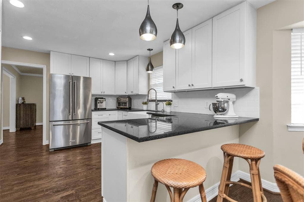 Modern kitchen featuring white cabinetry with black countertops, stainless steel French-door refrigerator, and pendant lighting with dark metal fixtures