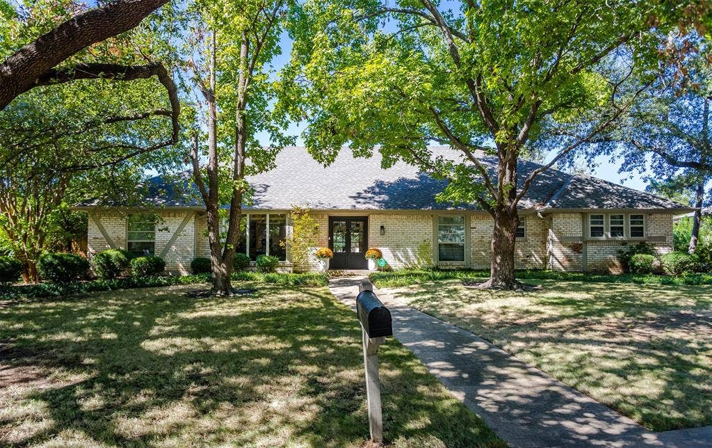 Charming single-story residence with a classic exterior featuring stone and stucco finishes, sheltered beneath mature oak trees