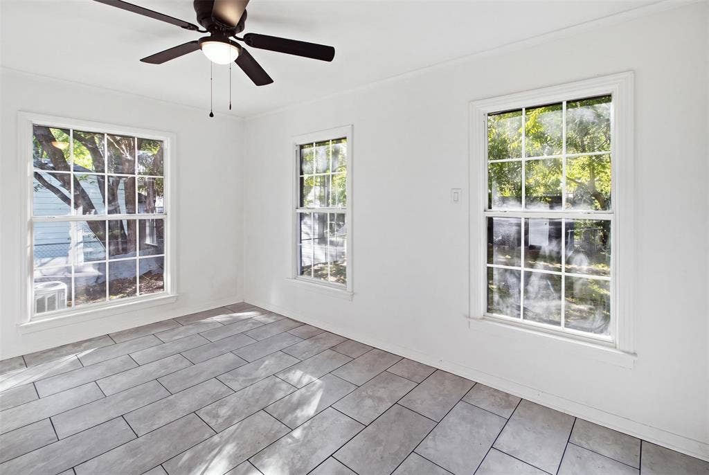 1105 Bell Drive, Greenville, TX 75401 Three bright windows with grid panes, a ceiling fan with light, and light-toned rectangular floor tiles