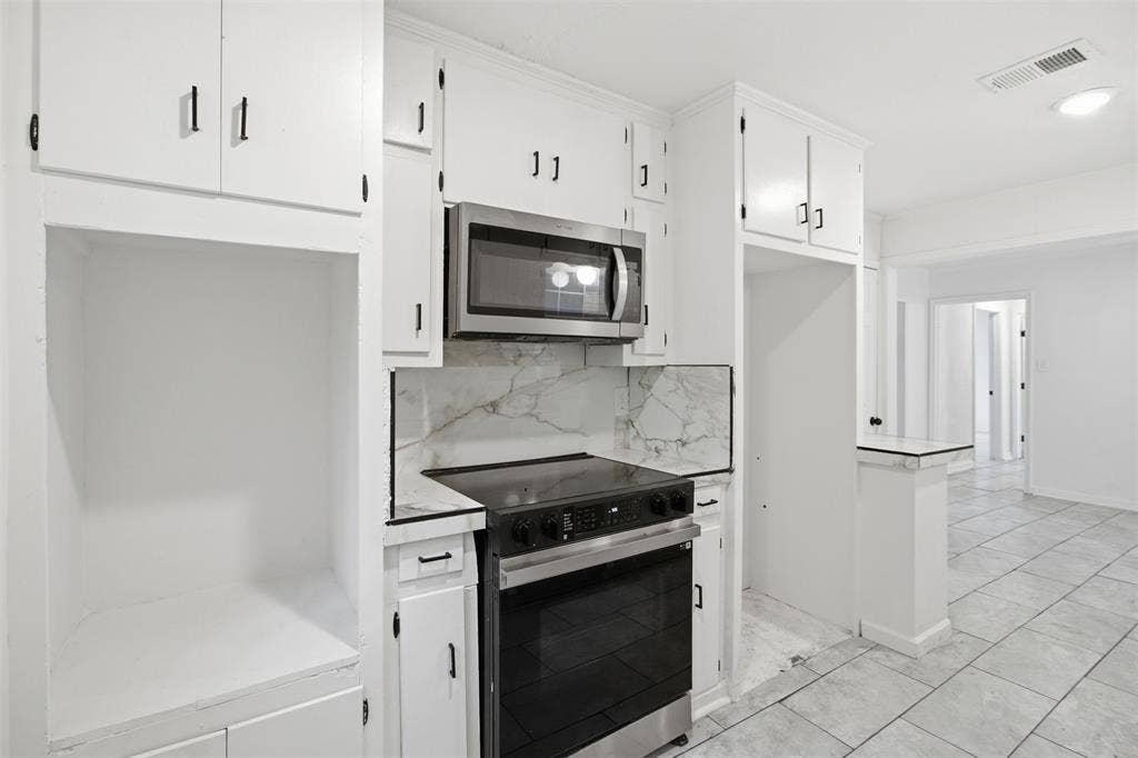 1105 Bell Drive, Greenville, TX 75401 White cabinetry with black hardware, stainless steel microwave, black electric range, marble-patterned backsplash, and tile flooring