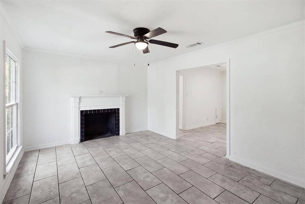 1105 Bell Drive, Greenville, TX 75401 Spacious living area featuring diagonal tile flooring, a fireplace with black surround, ceiling fan with integrated lighting, and abundant natural light from large windows