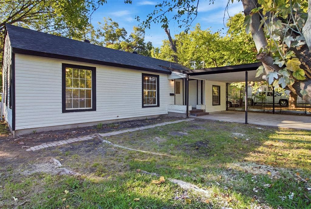1105 Bell Drive, Greenville, TX 75401 White horizontal siding exterior with black trim windows, a dark roof, and a covered carport