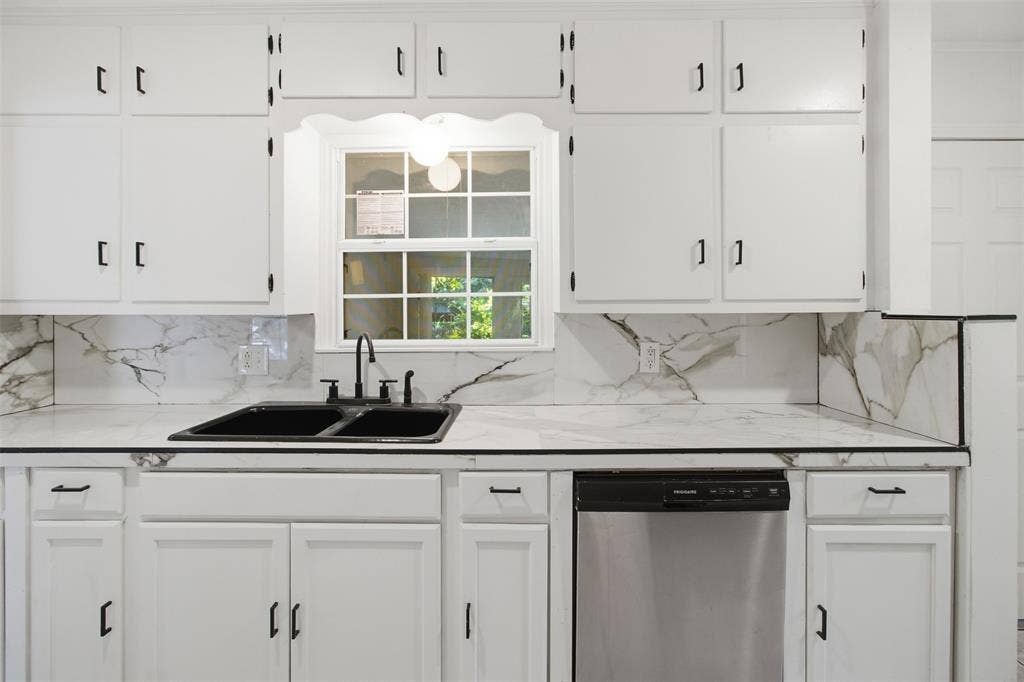 1105 Bell Drive, Greenville, TX 75401 White cabinetry with black hardware, white countertops with veining, a black double basin sink with a black faucet, and a stainless steel dishwasher