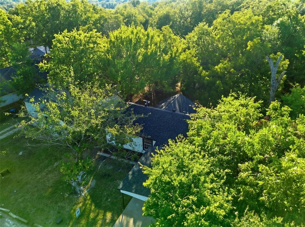 1105 Bell Drive, Greenville, TX 75401 Aerial view showcasing a dark-roofed residence nestled within mature, lush landscaping