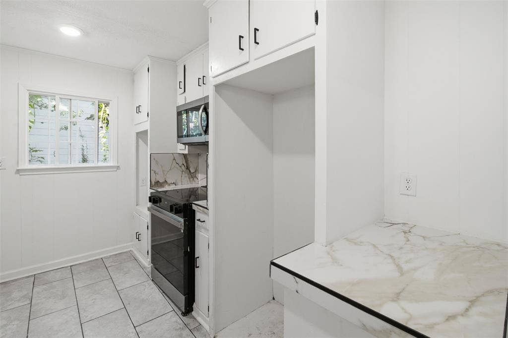 1105 Bell Drive, Greenville, TX 75401 White kitchen cabinetry with black hardware, stainless steel range and microwave, marbled countertops, and tile flooring