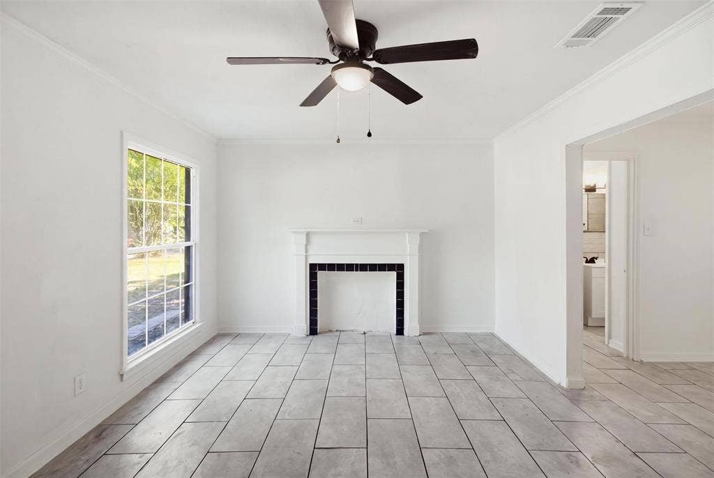 1105 Bell Drive, Greenville, TX 75401 Expansive room with tile flooring, a decorative fireplace, a multi-pane window, and a ceiling fan with integrated lighting