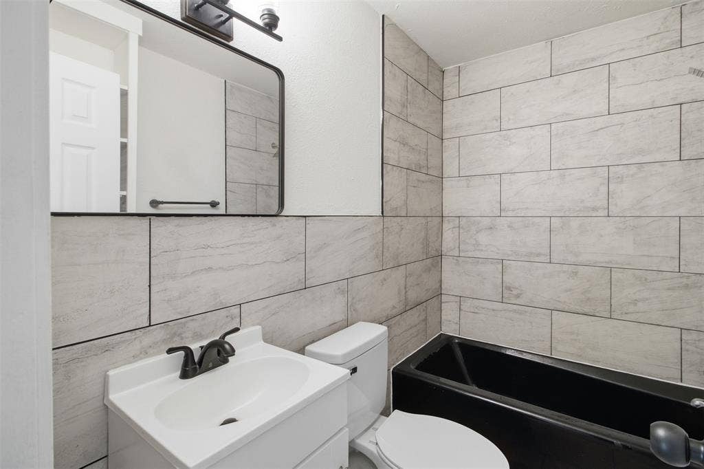 1105 Bell Drive, Greenville, TX 75401 Bathroom featuring a black bathtub, white vanity with integrated sink, and light-toned rectangular wall tiling