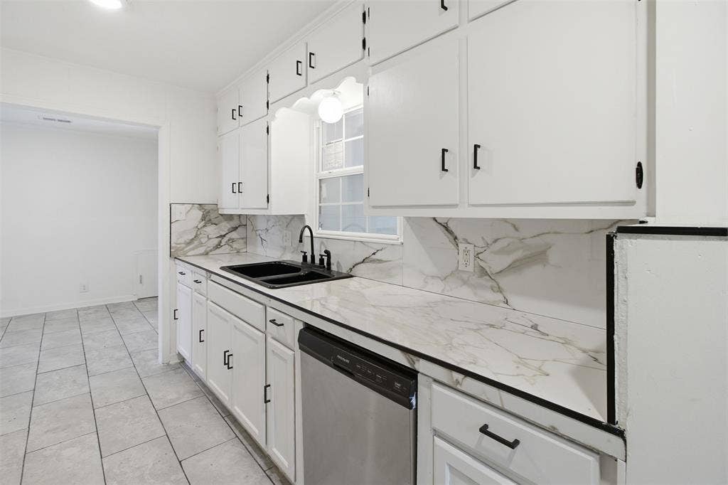 1105 Bell Drive, Greenville, TX 75401 White cabinetry with black hardware, marble-patterned countertops and backsplash, stainless steel dishwasher, black sink with black faucet, and tiled flooring
