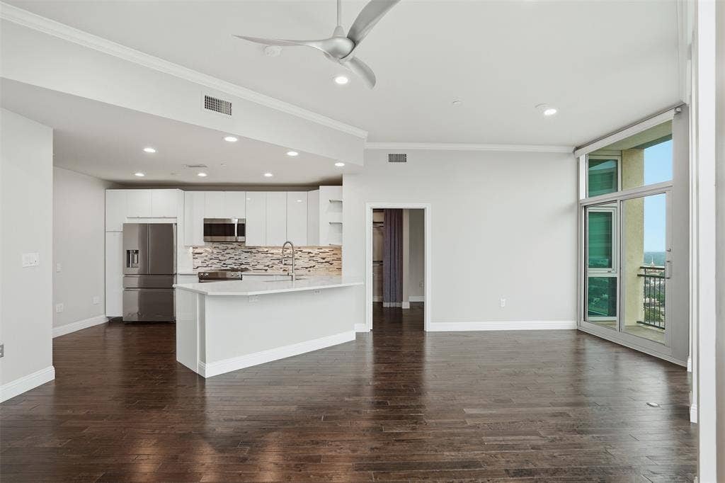 500 Throckmorton Street, #1605, Fort Worth, TX 76102 Hardwood flooring throughout, a kitchen featuring an island with a sink, white cabinetry, stainless steel appliances, and a tiled backsplash