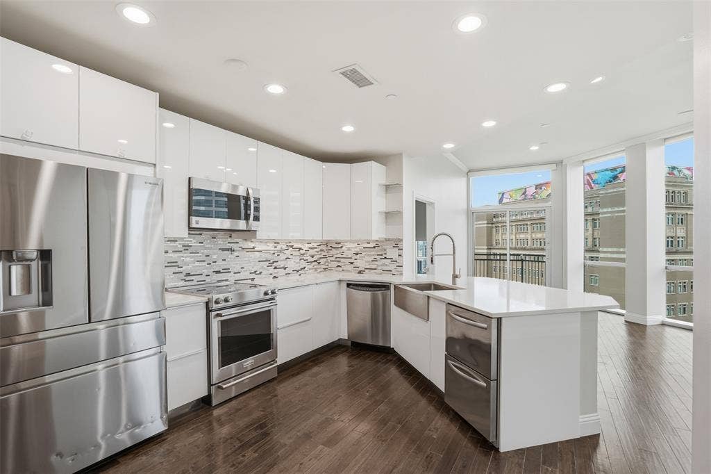 500 Throckmorton Street, #1605, Fort Worth, TX 76102 Sleek kitchen featuring white cabinetry, stainless steel appliances, a farmhouse sink, stone countertops, and wood-finish flooring