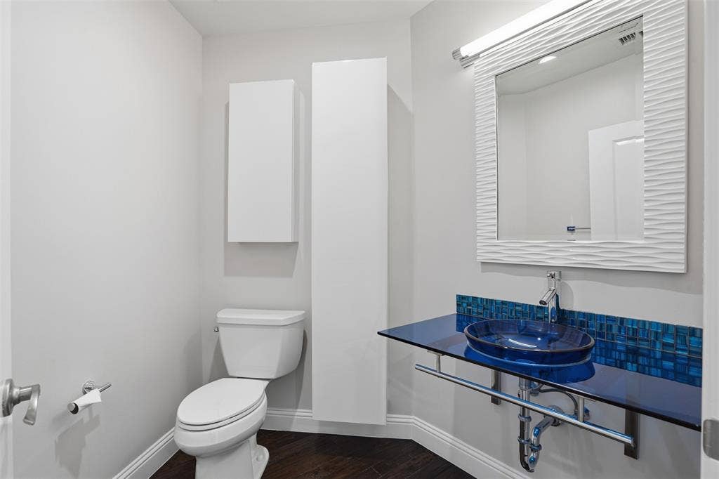 500 Throckmorton Street, #1605, Fort Worth, TX 76102 Powder room featuring a blue glass vessel sink, floating glass countertop, mosaic tile backsplash, and two wall-mounted storage cabinets
