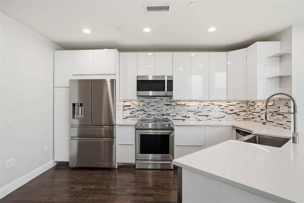 500 Throckmorton Street, #1605, Fort Worth, TX 76102 Modern kitchen featuring white flat-panel cabinetry, stainless steel appliances, a mosaic tile backsplash, and wood-finish flooring