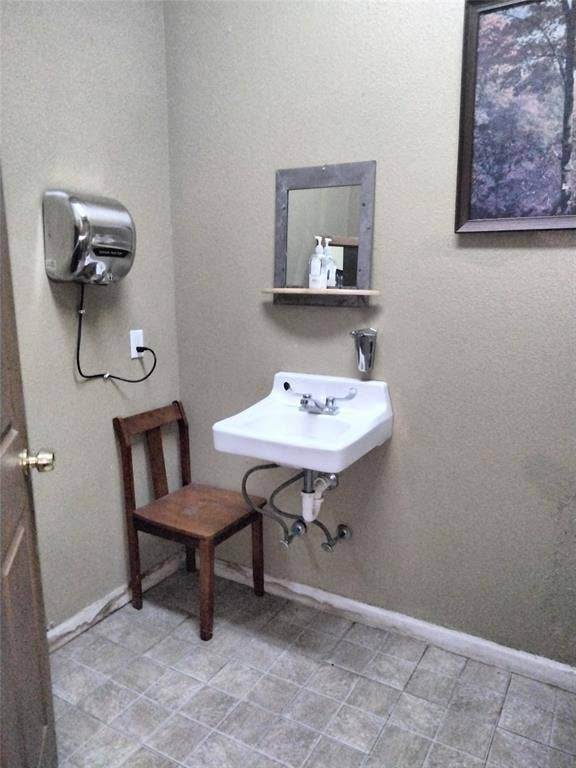 10424 County Road 1099, Princeton, TX 75407 White wall-mounted sink with chrome fixtures, framed mirror with integrated shelf, tiled flooring, and a wall-mounted hand dryer